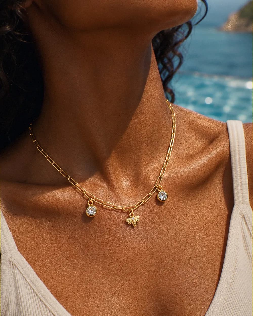Collier à charms dorés — abeille et deux cristaux ronds — porté au bord de la mer