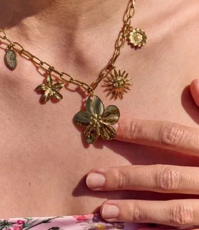 Collier à charms fleurs et soleil dorés porté sur la peau